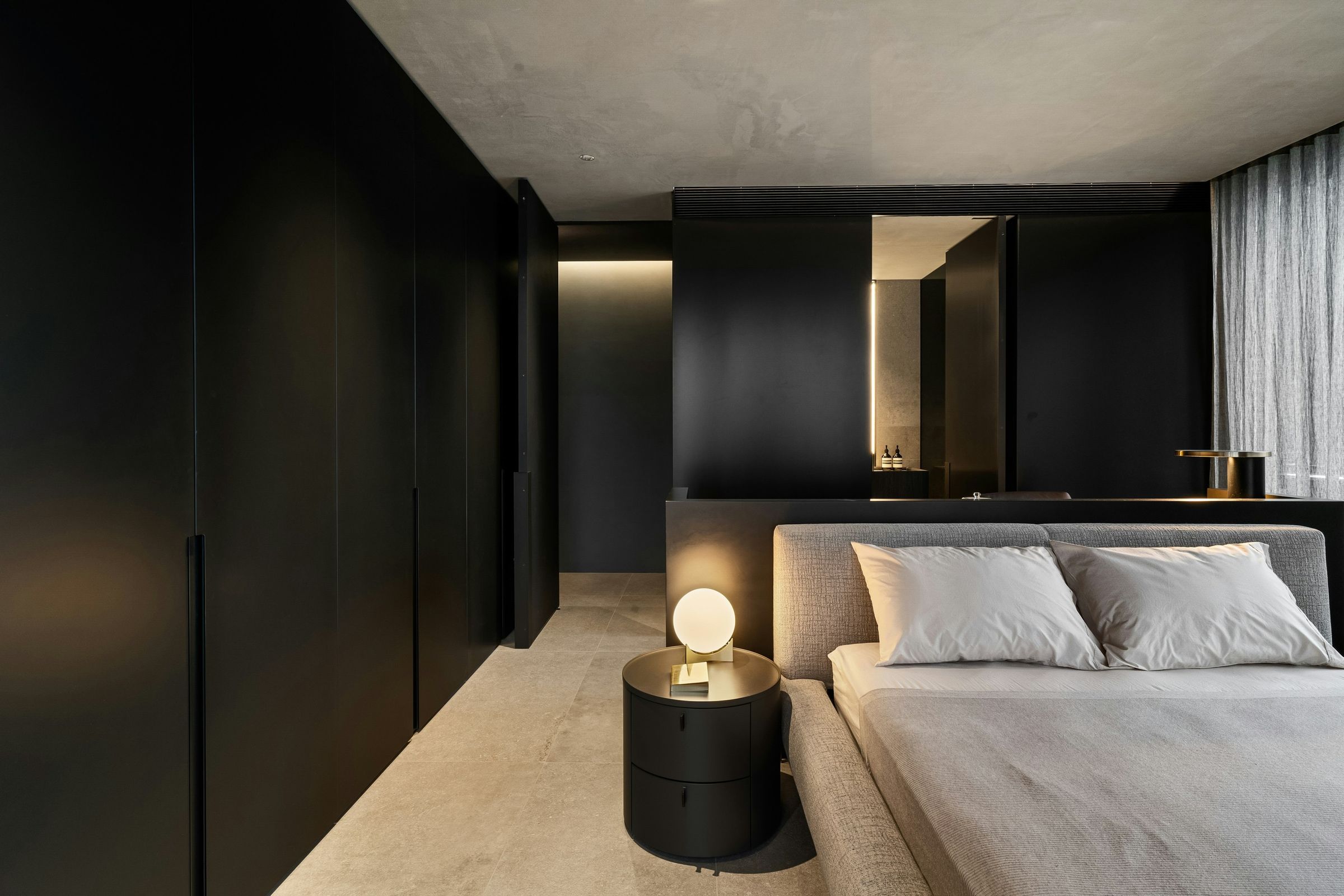 Sea suite at dusk: black joinery, stone floor and a single lit lamp by the bed