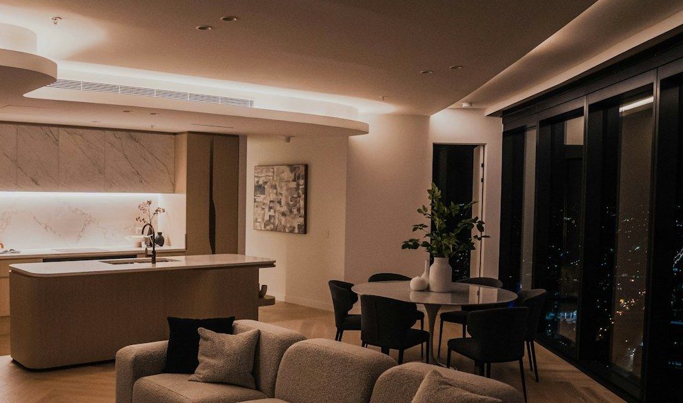 Open living room and kitchen in the evening, city lights behind floor-to-ceiling windows